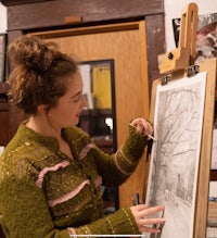 a woman is drawing on an easel in an art studio